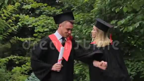 穿着学术服装在公园跳舞的快乐男女毕业典礼视频的预览图