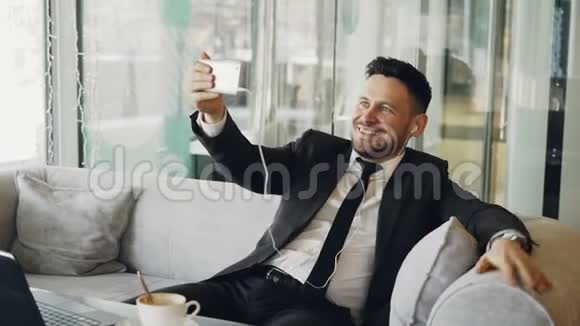穿着正式服装的白人商人微笑着用智能手机进行在线视频通话愉快地挥动着他的手视频的预览图