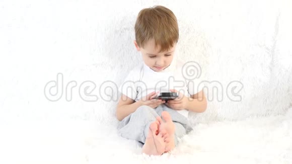 孩子坐在白色沙发上玩智能手机玩得很开心视频的预览图