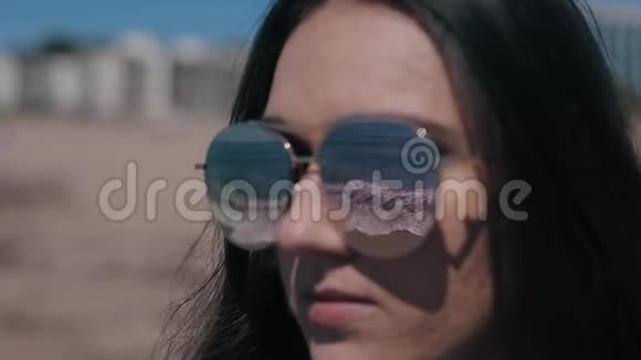 海滩上一个戴太阳镜的漂亮女孩的特写肖像太阳眼镜里反射着波浪的大海视频的预览图