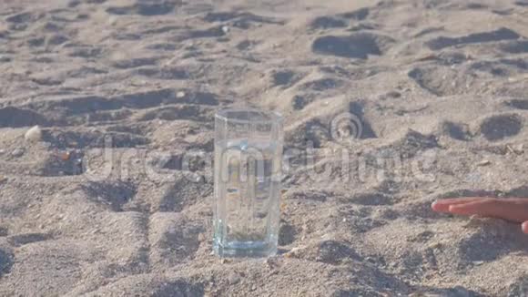 女人手伸向一个盛满水的玻璃杯它站在沙子的中间视频的预览图