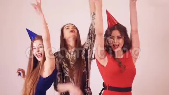 派对上的女孩在跳舞三个漂亮的女孩跳舞唱歌派对上穿着漂亮裙子的女人空中亲吻派对帽视频的预览图