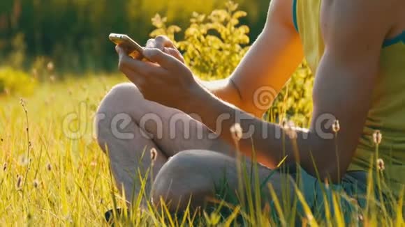 年轻人看着智能手机在美丽的夏天的背景下绿色的草地上印着一些东西视频的预览图