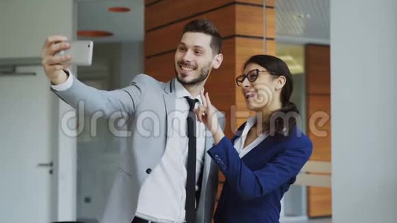 快乐的商人和他的女同事在现代办公室的社交媒体上用智能手机相机自拍视频的预览图