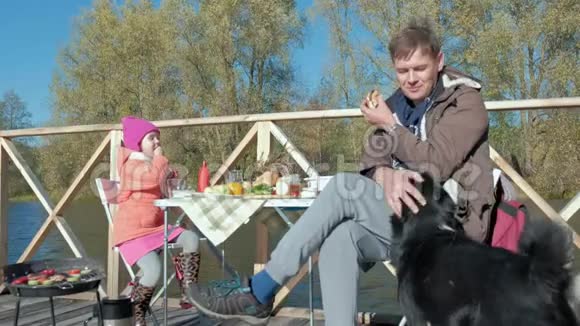 父亲和女儿成熟的男人和小女孩穿着温暖的衣服坐在桌子旁吃东西在烤架上煮蔬菜视频的预览图