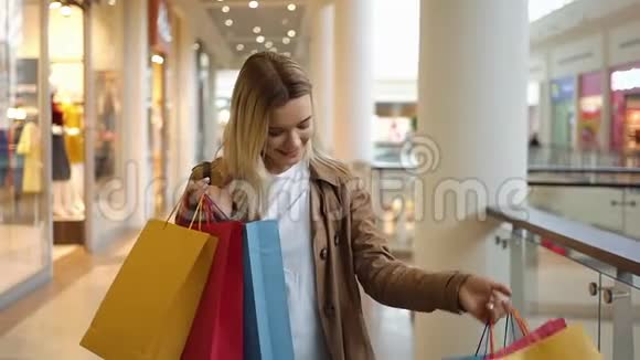 快乐的金发女人看着她站在商场里的彩色纸袋视频的预览图