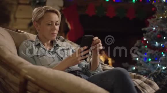 圣诞夜成年女性在智能手机上用装饰好的树发短信视频的预览图