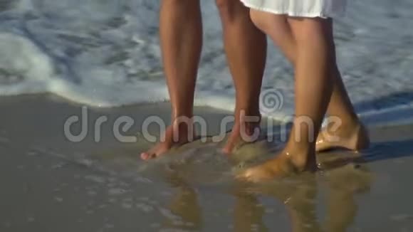 年轻漂亮的夫妇走在海边男孩和女孩他们很开心阳光灿烂慢动作双脚视频的预览图
