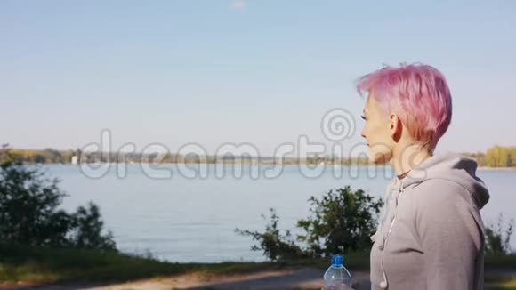 粉红头发的年轻女士在湖边慢跑视频的预览图