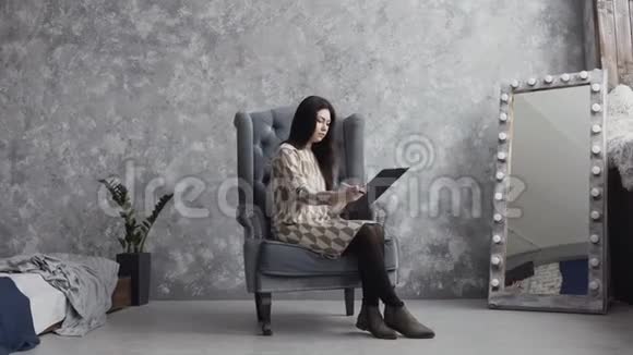 一个可爱的女孩坐在家里的软扶手椅上用阴影调色板在水彩纸上作画视频的预览图