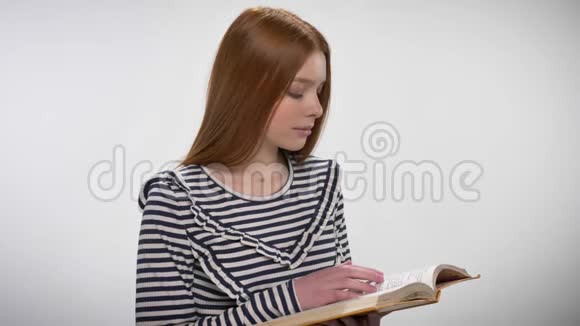 年轻甜美沉稳的姜姑娘正在看书看着镜头白色背景视频的预览图