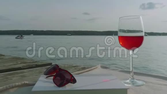 日落时可以在背景上看到一杯红酒太阳镜和一本书从左到右摄像机移动视频的预览图