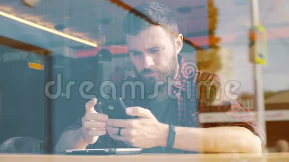 在咖啡馆的智能手机上使用应用程序的人从窗户射中视频的预览图