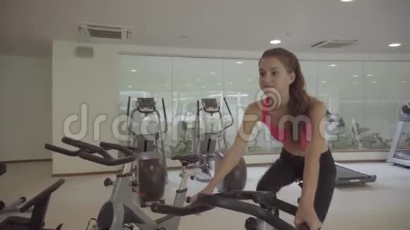 在健身房骑运动自行车的女人骑自行车运动的女性视频的预览图
