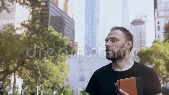 站在公园里靠近美国纽约的办公室和摩天大楼的年轻快乐商人的肖像视频的预览图