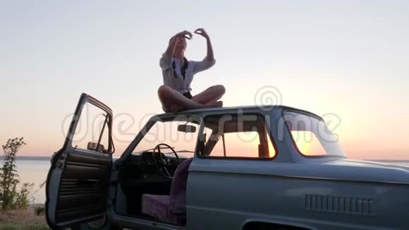 女孩在户外汽车屋顶冥想女性在日落时在背景海的汽车上缓慢运动冥想快乐视频的预览图