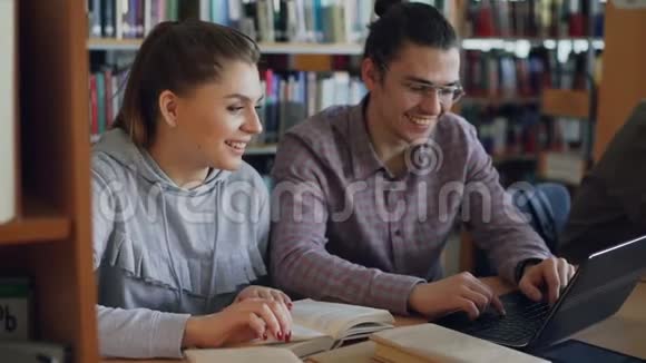 性格开朗的男女大学生一起在笔记本电脑上工作坐在大学图书馆的桌子上视频的预览图