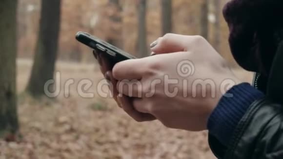 在秋天的公园里用智能手机关闭女人的手秋天在森林里散步的女孩的生活方式概念视频的预览图