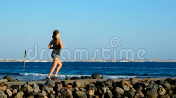 运动女孩沿着石头小径跑向大海布鲁内特看着远方做梦视频的预览图