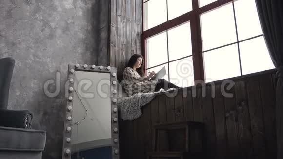 灵感女艺术家穿着靠近窗户的裙子迷人的黑发女孩坐在艺术的窗台上视频的预览图