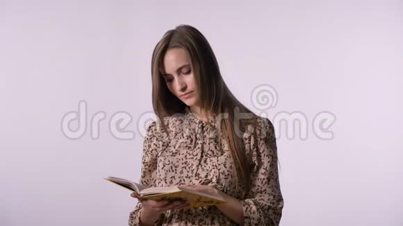 年轻漂亮的女人正在看书看着摄像机微笑着白色的背景视频的预览图