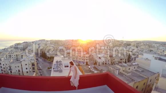 美丽的女孩坐在城市背景的屋顶上为摄影师摆姿势的女孩空中景观视频的预览图
