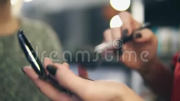 专业化妆师双手用特殊的刷子在年轻女性的皮肤上涂抹面部模糊特写镜头视频的预览图