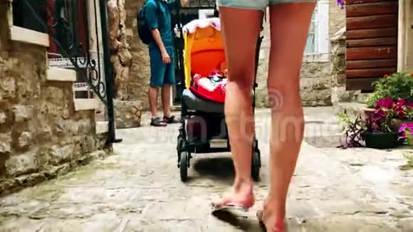 妈妈和她的孩子带着婴儿车沿着狭窄的老街旅行视频的预览图