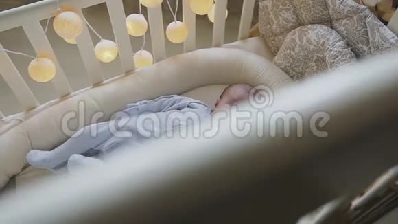 出生的小男孩躺在婴儿床上看着相机微笑着可爱的小婴儿躺在家里的婴儿床上小男孩视频的预览图
