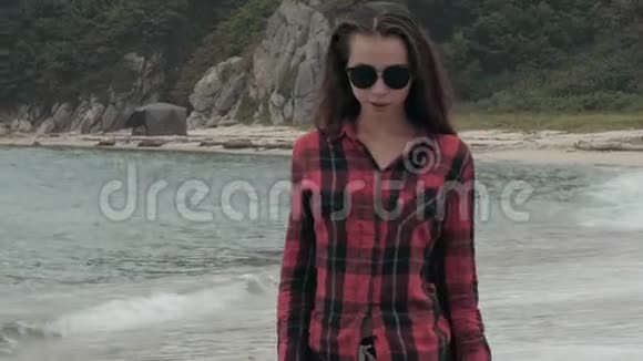 阴天时穿着格子衬衫在沙滩上漫步的年轻漂亮的欧洲女孩视频的预览图