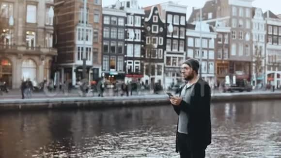 4K卡索人戴着智能手机的帽子英俊的胡子创意商人在河堤上发短信视频的预览图