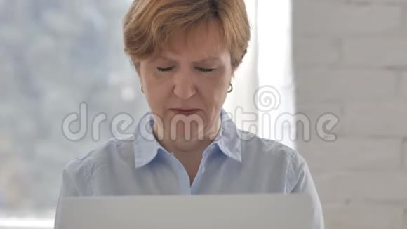 头痛紧张的老妇人在笔记本电脑上工作视频的预览图
