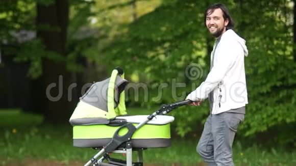 一位年轻的父亲带着婴儿车在公园里散步有新生婴儿的男人亲子关系嬉皮士父亲节视频的预览图