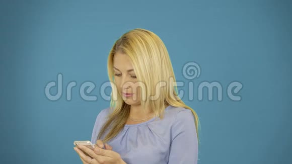 女士在蓝色背景下在智能手机上打字写信息年轻漂亮的女人站着用手机视频的预览图