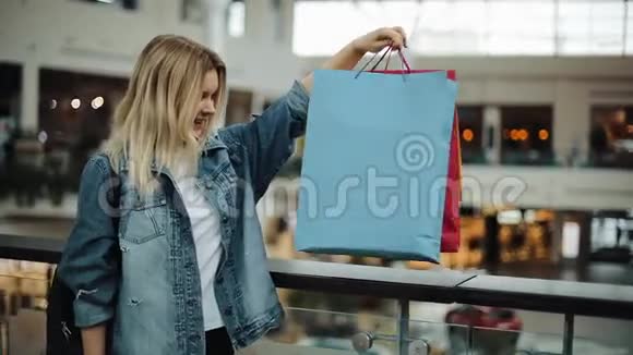 快乐的金发女孩看着站在购物中心的五颜六色的购物袋视频的预览图