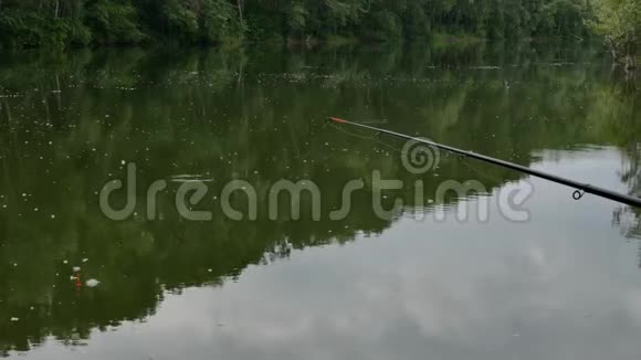 钓鱼竿在平静的湖面上等待叮咬周末在水上4K云和树的倒影视频的预览图