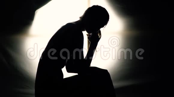 一个疲惫的女孩坐在黑暗中慢动作的剪影视频的预览图