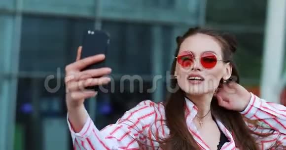 年轻漂亮的红墨镜模特在智能手机上自拍视频的预览图
