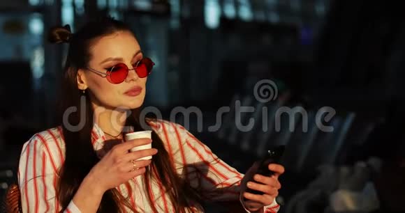 戴着红色太阳镜的迷人年轻女子在傍晚的阳光下喝咖啡视频的预览图