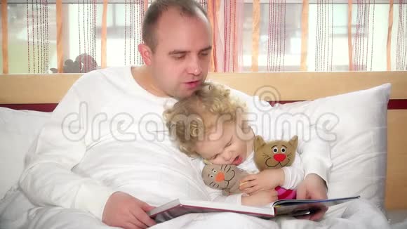 可爱的女孩睡着了而爱的父亲在床上看书视频的预览图