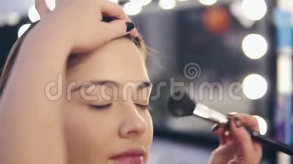 专业化妆师在工作中用女性手在年轻女性皮肤上涂抹面部粉末特写视频的预览图