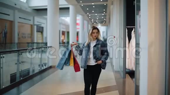 一位体贴的金发女郎带着袋子走在商场的橱窗前视频的预览图