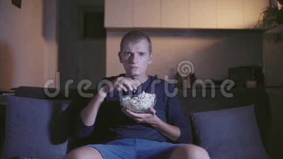成人男子有兴趣看电视和电影坐在舒适的沙发上吃美味的爆米花在碗里手工夜晚视频的预览图