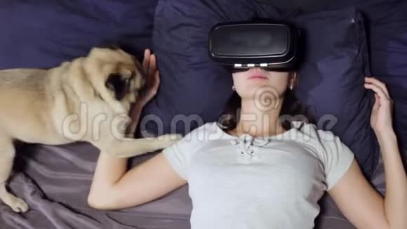 躺在床上枕头上的年轻女性的俯视图使用虚拟现实观看VR视频视频的预览图