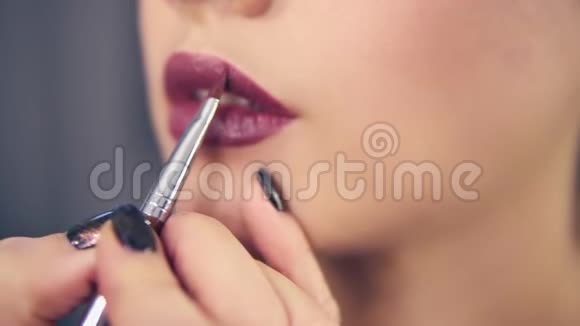 专业化妆师用特殊的刷子在模特的嘴唇上涂口红或唇彩的特写视频的预览图