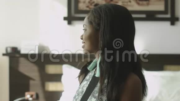 一位黑发年轻的非裔美国妇女坐在时尚酒店房间的沙发上的肖像视频的预览图