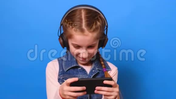 戴着耳机在智能手机上玩电子游戏的年轻女孩视频的预览图