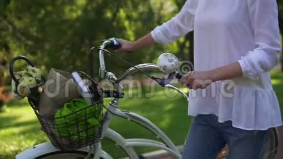 女人的近景她手里拿着一辆城市自行车的车把手里拿着一个花篮和一本书女人享受着视频的预览图