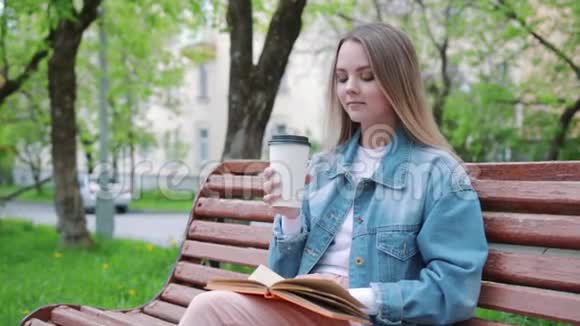 年轻的黑发女孩坐在长凳上喝咖啡看书视频的预览图