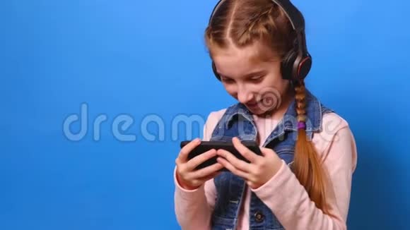 戴着耳机在智能手机上玩电子游戏的小女孩视频的预览图